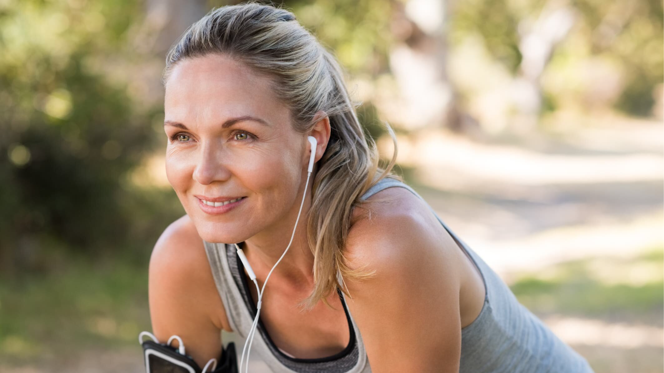 A woman taking a break from exercising outdoors, smiling and looking energized.