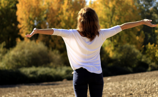 Back view of a woman standing outdoors with open arms, embracing nature and feeling relaxed