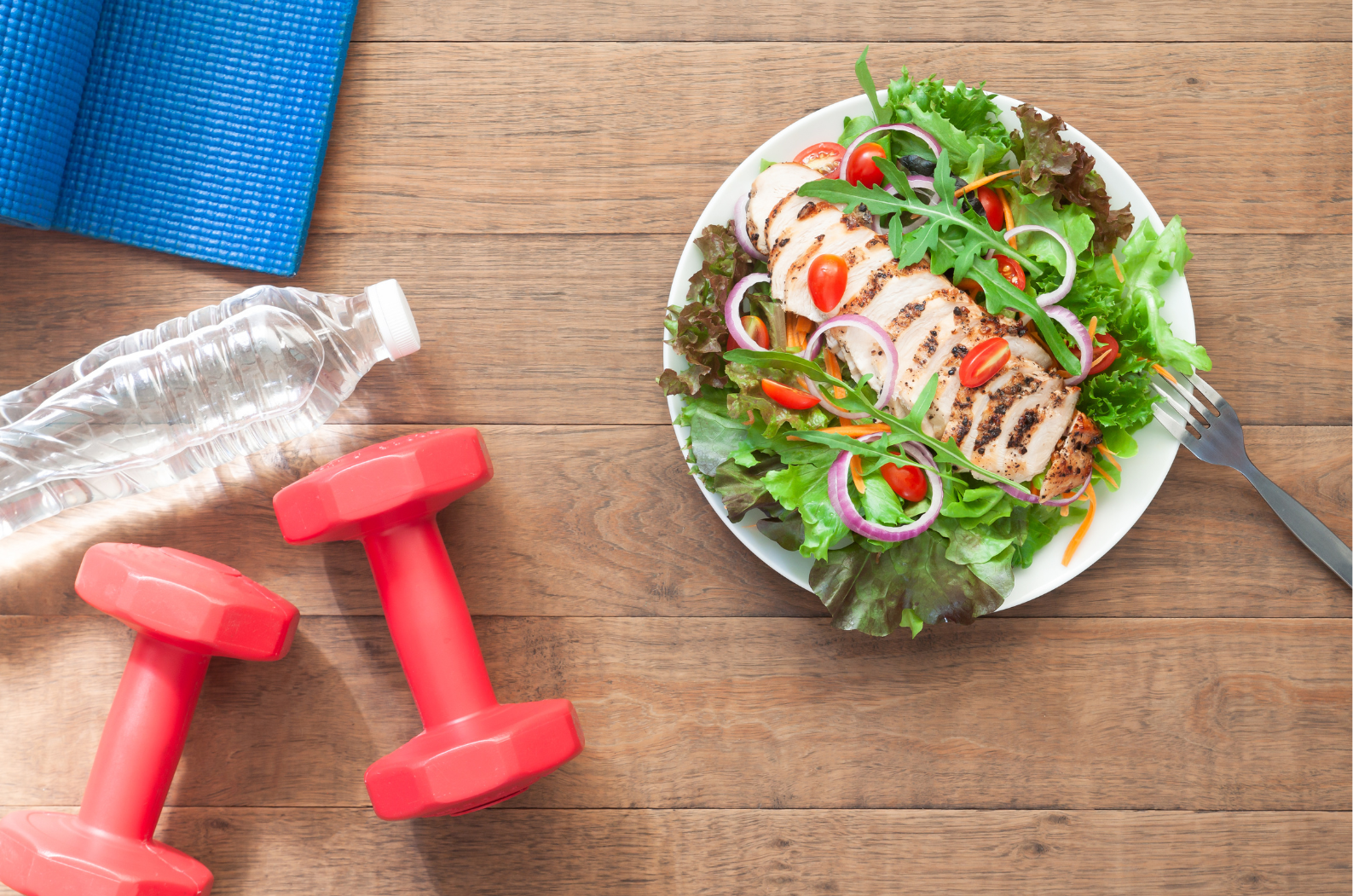 Fresh salad with avocado, water bottle, and red dumbbells on a wooden table, symbolizing a healthy and active lifestyle.