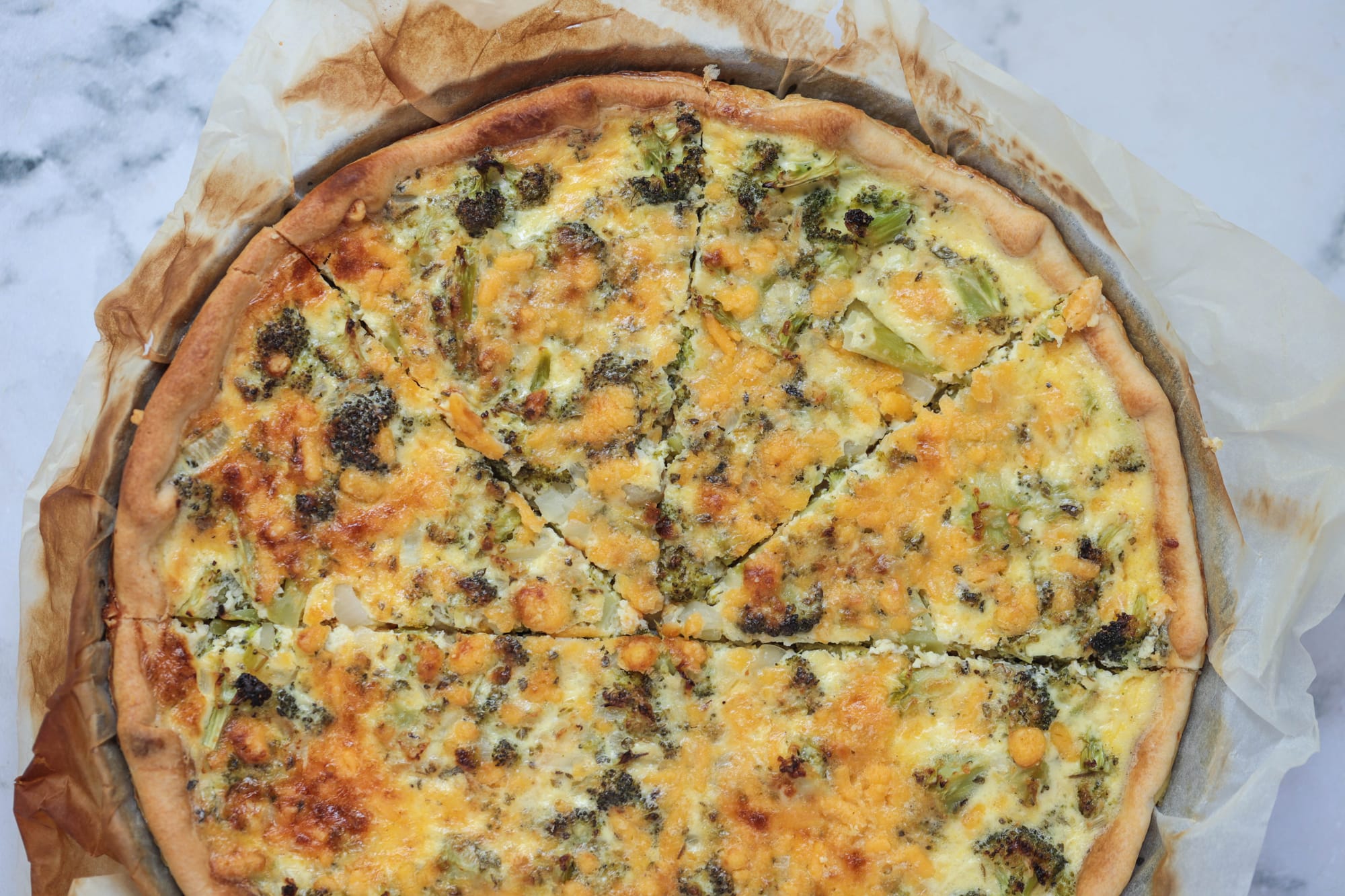 Golden broccoli cheddar quiche with a flaky crust, fresh broccoli, and melted cheese, freshly baked and sliced for serving