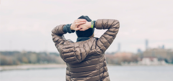 Person in a puffer jacket looking over a calm lake, symbolizing stress relief and reflection in a peaceful environment