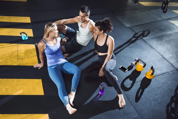 People sitting on a gym floor, engaging in a post-workout conversation, reflecting the importance of movement for health.