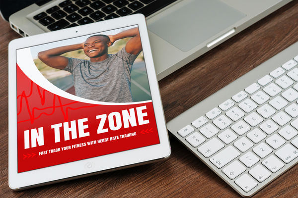 Tablet displaying the In The Zone heart rate training guide, with a smiling man on the cover next to a laptop and keyboard