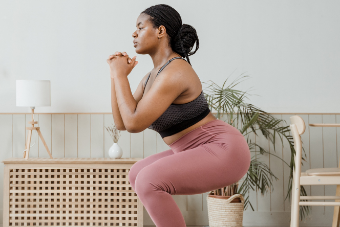 Woman performing a squat exercise indoors, demonstrating proper squat form for muscle engagement and joint safety.