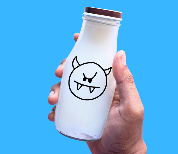 Hand holding a milk bottle with a cartoon devil face, representing calcium's "bad" effect on iron absorption in the body.