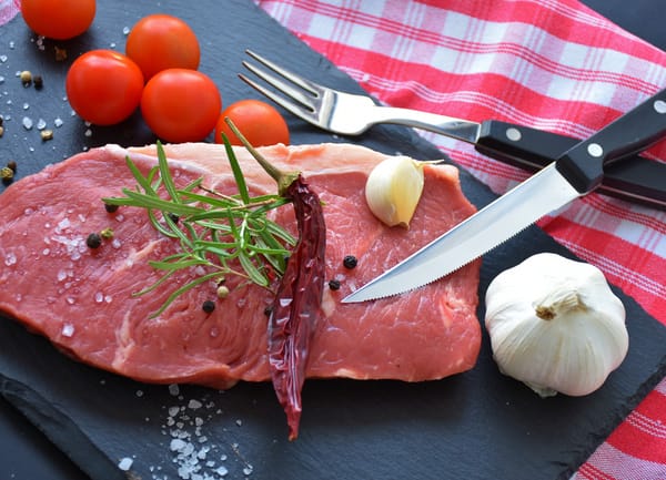 A raw steak garnished with fresh herbs, garlic, and tomatoes, ready for a protein-rich meal.