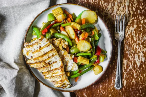 Grilled chicken breast served with a colorful medley of sautéed vegetables on a rustic plate.