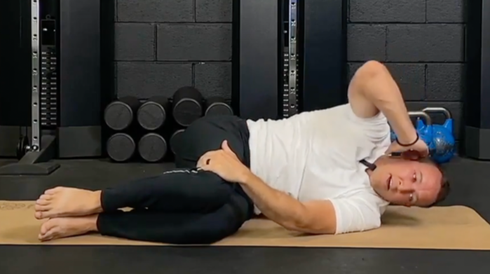 Person performing an upper back mobility exercise on a yoga mat in a gym setting.