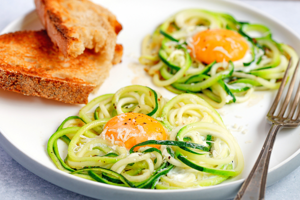 Zucchini egg nests with grated Parmesan and egg yolks, served with toasted bread on a white plate.