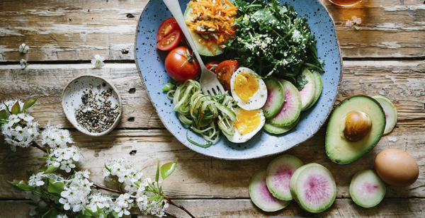 A healthy keto and low-carb meal with avocado, eggs, greens, and zucchini noodles on a rustic wooden table.