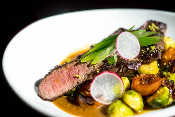 Juicy medium-rare steak with roasted Brussels sprouts, carrots, and radish garnish on a white plate with rich brown sauce.