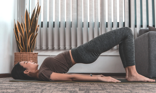 Woman performing a glute bridge exercise on a yoga mat, engaging her core and glutes for strength and stability.